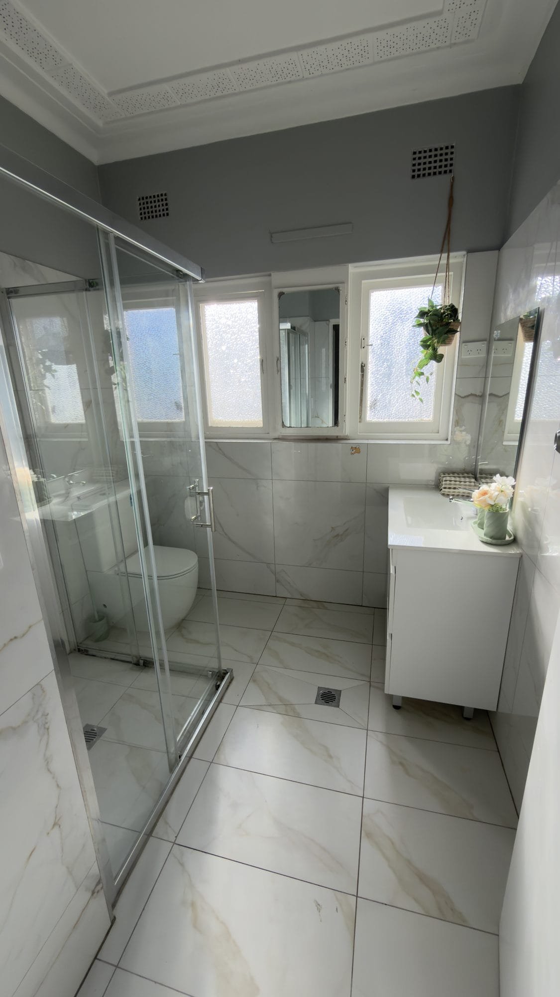 Renovated bathroom with a marble-look vanity, basin and a glass shower screen