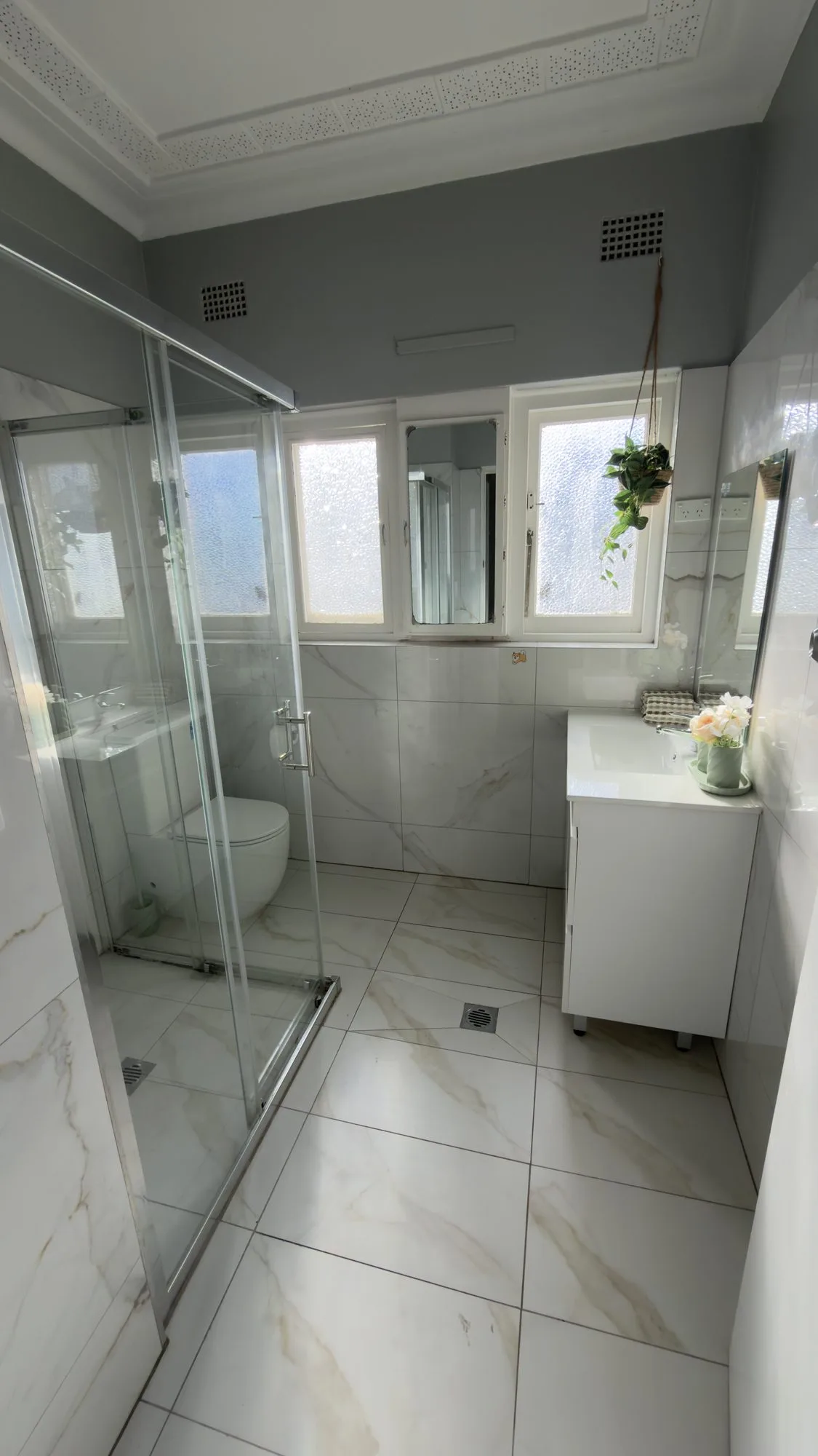 Renovated bathroom with a marble-look vanity, basin and a glass shower screen