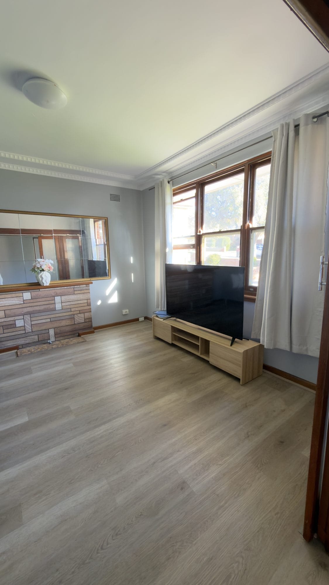 Shared living room with a television and a large window with light curtains