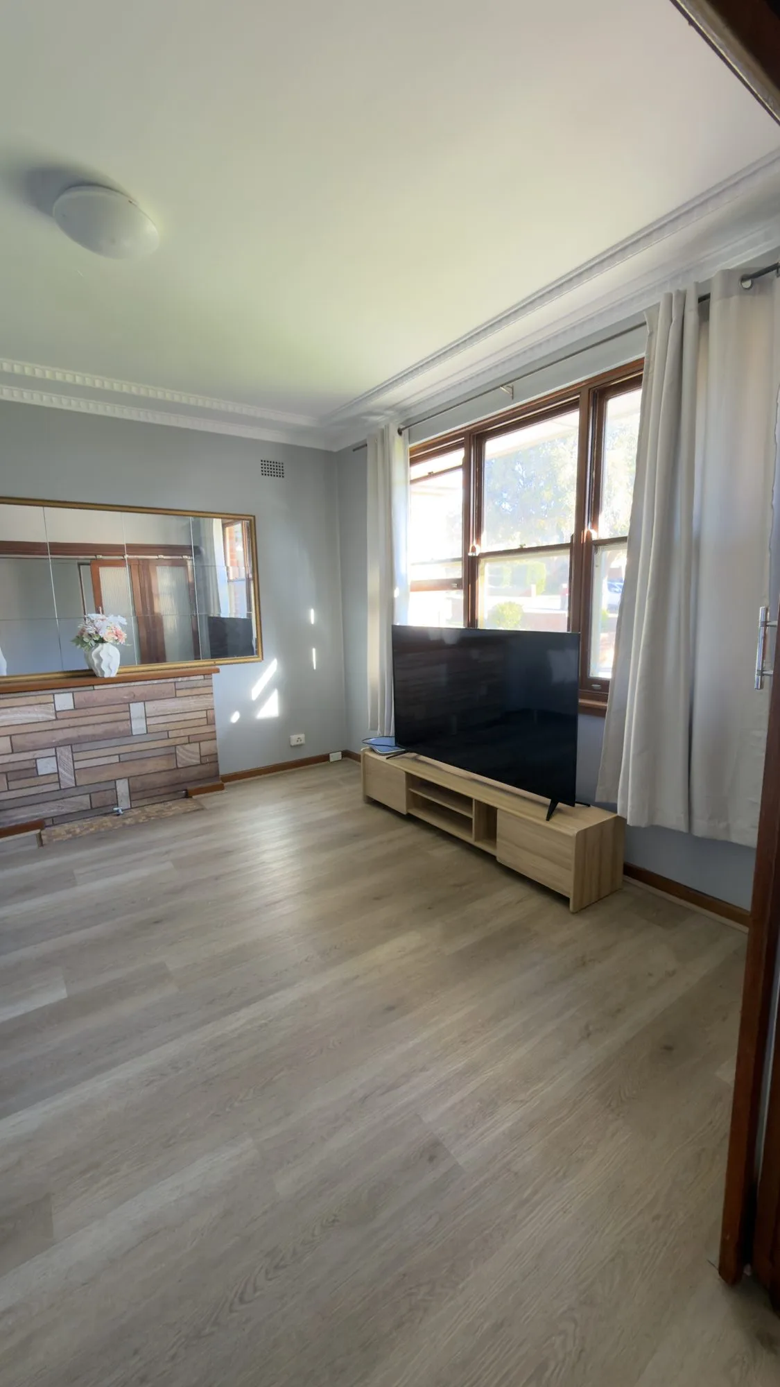 Shared living room with a television and a large window with light curtains